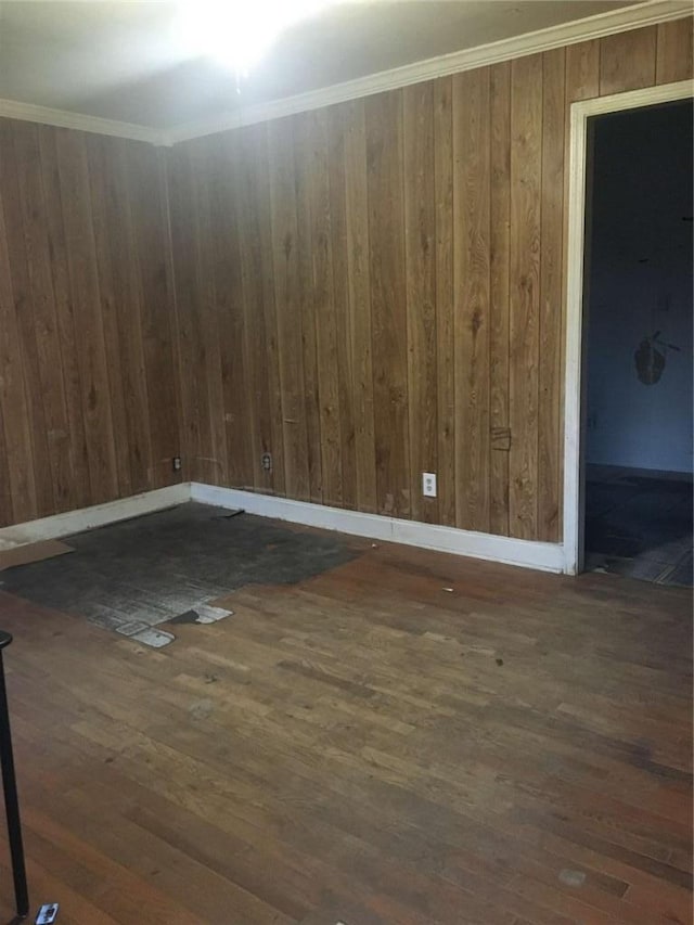 spare room featuring wood walls, baseboards, wood-type flooring, and ornamental molding