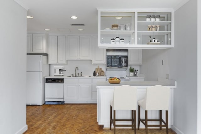 kitchen featuring parquet flooring, white cabinetry, sink, a kitchen breakfast bar, and white appliances