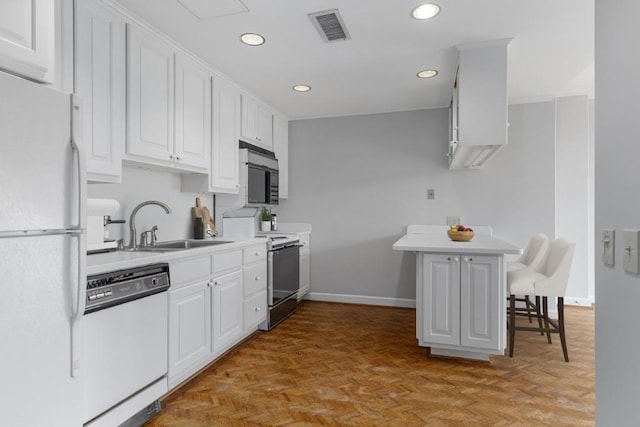 kitchen with white cabinetry, white appliances, light parquet flooring, and a kitchen bar