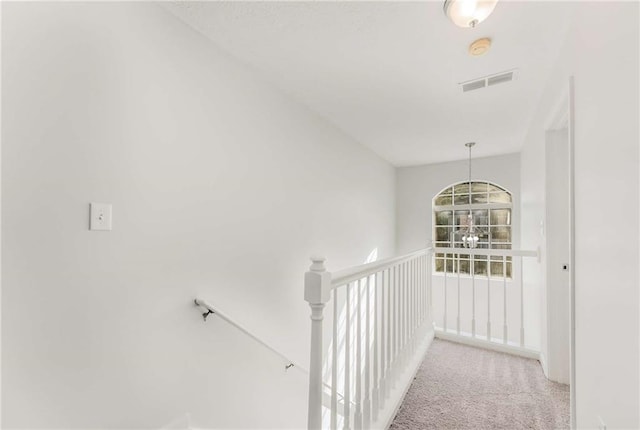 hallway featuring carpet, visible vents, and an upstairs landing