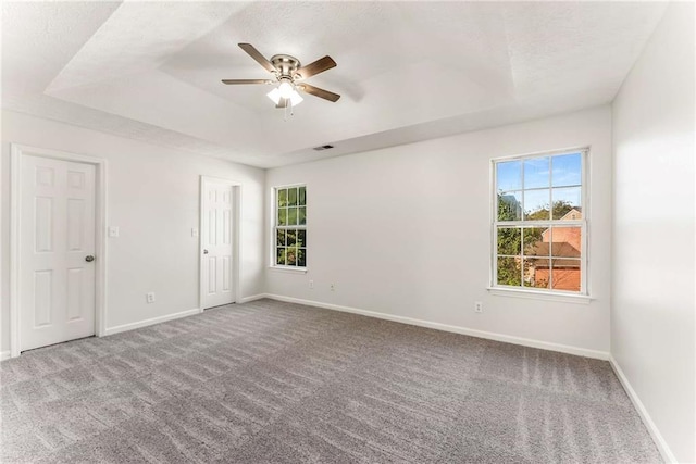 carpeted spare room with baseboards, visible vents, a tray ceiling, and a ceiling fan