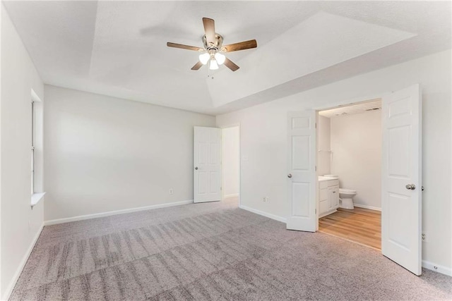 unfurnished bedroom with a raised ceiling, carpet flooring, baseboards, and ensuite bathroom