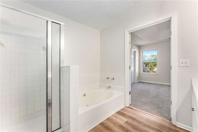 full bathroom with a stall shower, baseboards, wood finished floors, a textured ceiling, and a bath