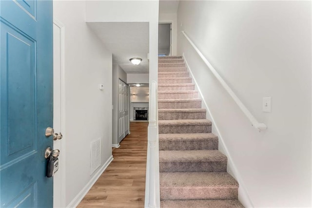 stairway featuring a fireplace, wood finished floors, visible vents, and baseboards