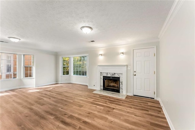 unfurnished living room featuring a textured ceiling, a fireplace, wood finished floors, baseboards, and ornamental molding