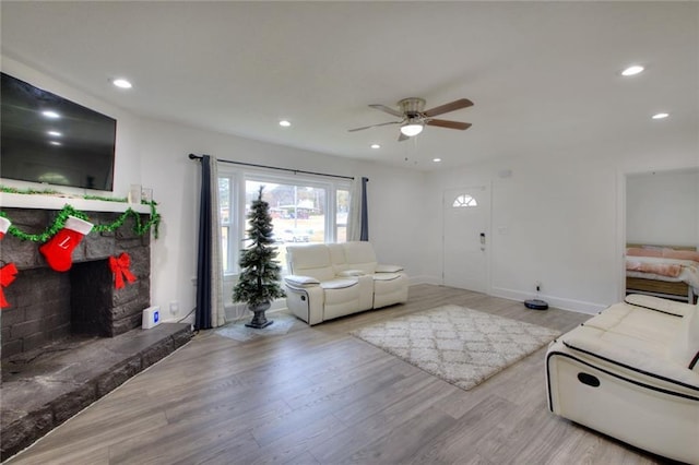 living room featuring light wood-type flooring, a stone fireplace, and ceiling fan