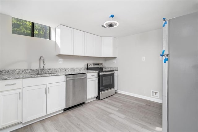 kitchen with white cabinets, light stone countertops, stainless steel appliances, light wood-style floors, and a sink