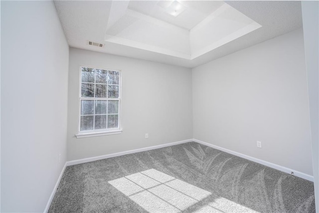 spare room with a tray ceiling, carpet, visible vents, and baseboards