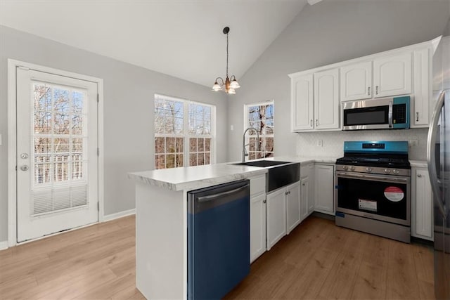 kitchen with sink, appliances with stainless steel finishes, kitchen peninsula, pendant lighting, and white cabinets