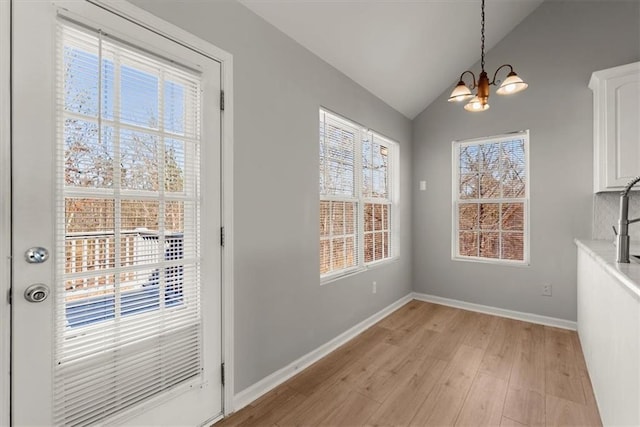 unfurnished dining area with lofted ceiling, a notable chandelier, and light wood-type flooring