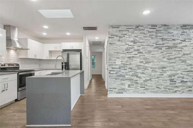 kitchen with white cabinetry, sink, stainless steel appliances, a center island with sink, and wall chimney exhaust hood