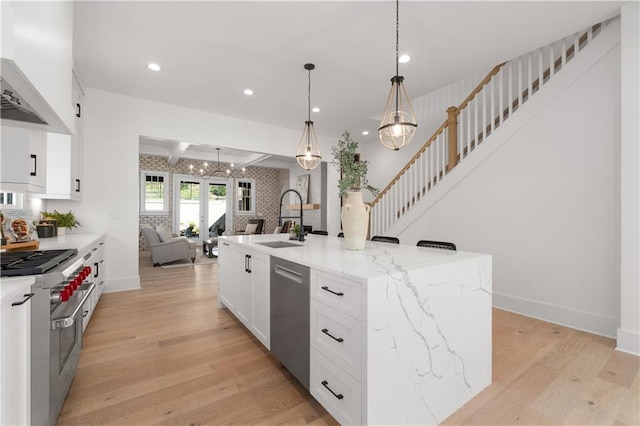 kitchen featuring appliances with stainless steel finishes, decorative light fixtures, sink, a kitchen island with sink, and light stone countertops