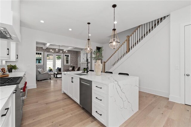 kitchen featuring sink, white cabinetry, light stone counters, hanging light fixtures, and an island with sink