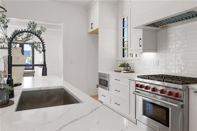 kitchen with stainless steel appliances, custom exhaust hood, light stone countertops, and white cabinetry