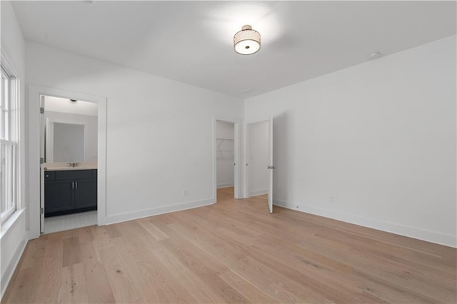 unfurnished bedroom featuring connected bathroom, a walk in closet, a closet, and light wood-type flooring