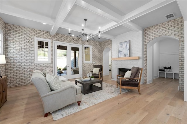 living room featuring french doors, brick wall, a brick fireplace, and light wood-type flooring