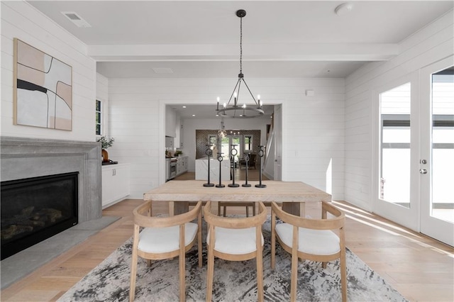 dining area with beam ceiling, a high end fireplace, light hardwood / wood-style floors, and french doors