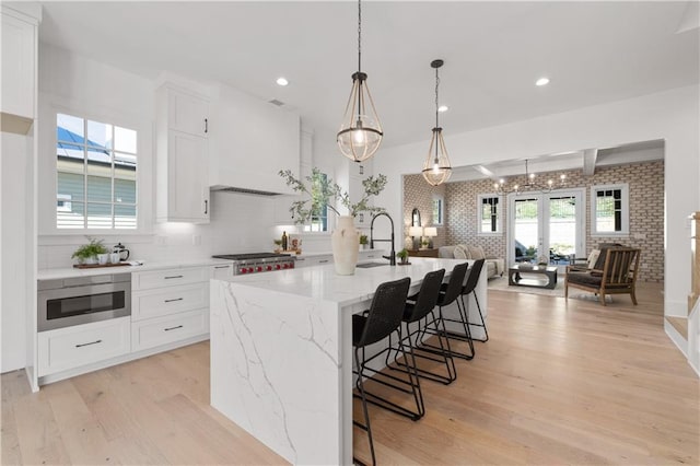 kitchen with stainless steel microwave, light stone counters, white cabinets, a center island with sink, and decorative light fixtures