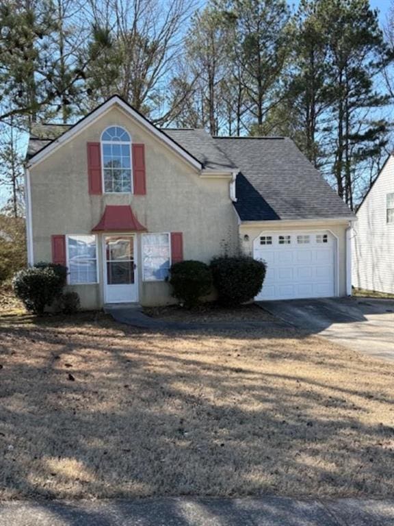 traditional-style house with an attached garage, a shingled roof, concrete driveway, and stucco siding