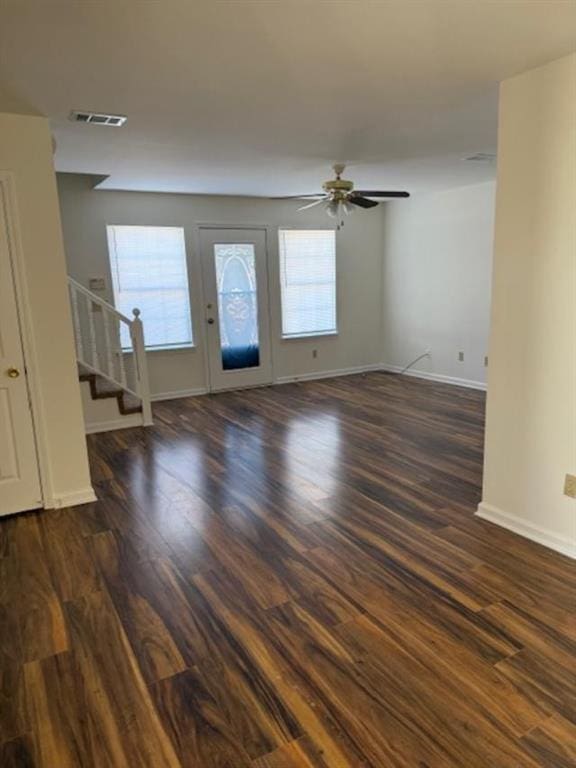 unfurnished living room with dark wood-style flooring, visible vents, ceiling fan, and stairway