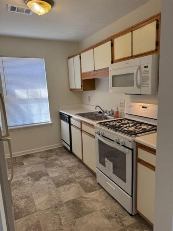 kitchen featuring white appliances, a sink, visible vents, baseboards, and light countertops