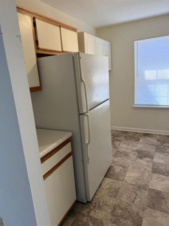 kitchen with baseboards, stone finish floor, freestanding refrigerator, light countertops, and white cabinetry