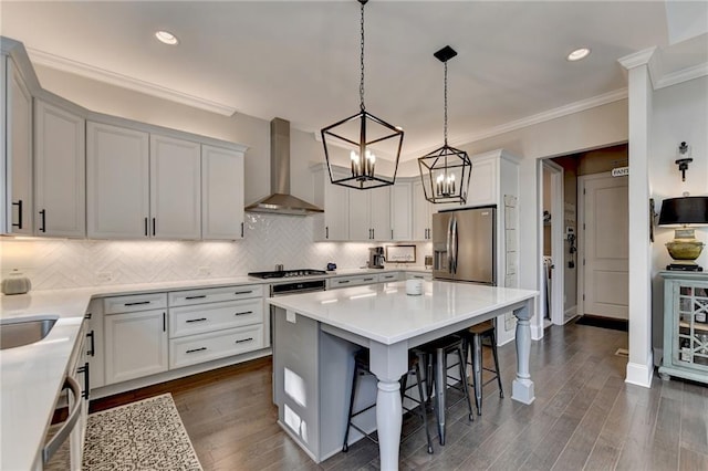 kitchen featuring appliances with stainless steel finishes, a kitchen bar, a center island, wall chimney exhaust hood, and decorative light fixtures