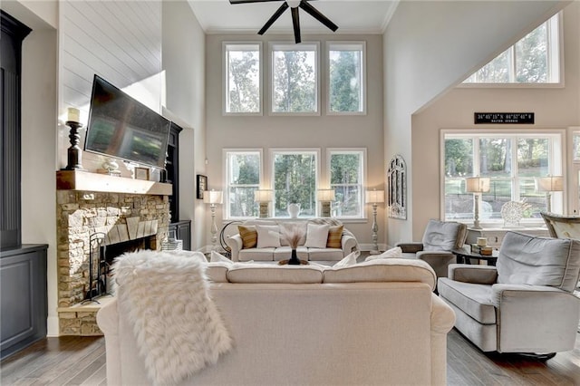 living room with ceiling fan, a stone fireplace, a towering ceiling, and light hardwood / wood-style flooring