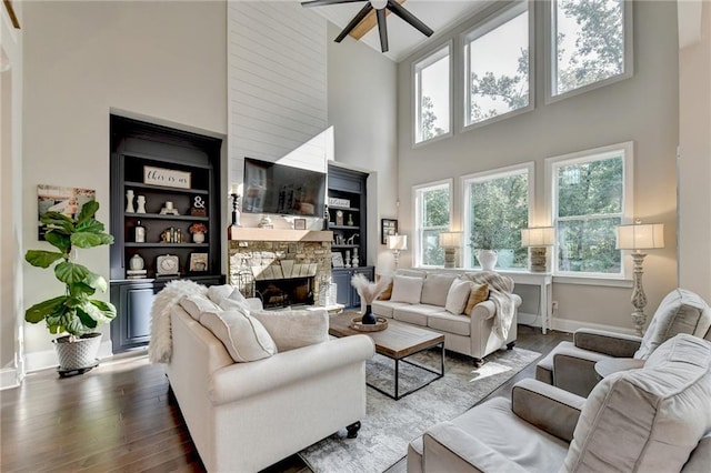 living room featuring ceiling fan, high vaulted ceiling, dark hardwood / wood-style flooring, and a stone fireplace