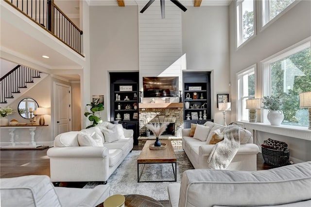 living room featuring a towering ceiling, a stone fireplace, ceiling fan, beamed ceiling, and hardwood / wood-style flooring