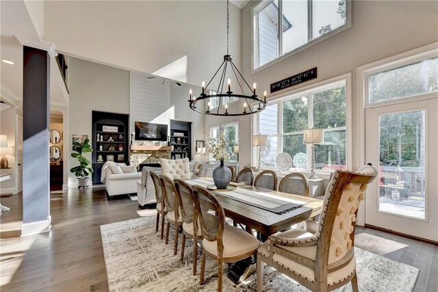 dining area with a fireplace, dark hardwood / wood-style floors, a chandelier, and a high ceiling