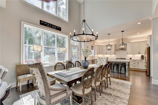 dining area with a towering ceiling, sink, dark wood-type flooring, a notable chandelier, and ornamental molding