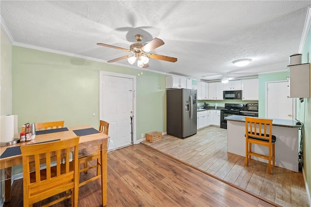 kitchen with light wood-type flooring, ornamental molding, a textured ceiling, black appliances, and white cabinets