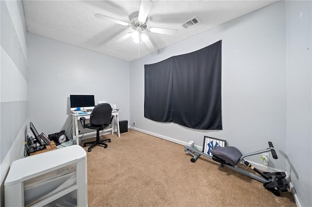 carpeted home office with ceiling fan and a textured ceiling