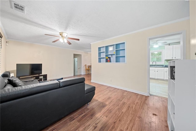 living room featuring wood-type flooring, a textured ceiling, crown molding, and sink