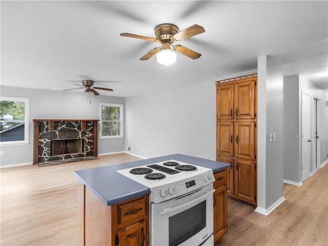 kitchen with light hardwood / wood-style floors, ceiling fan, a fireplace, a kitchen island, and white range with electric cooktop