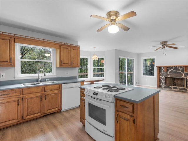 kitchen with decorative light fixtures, sink, white appliances, light wood-type flooring, and a stone fireplace