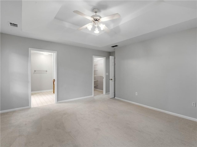 unfurnished bedroom with a spacious closet, ceiling fan, a tray ceiling, a closet, and light colored carpet