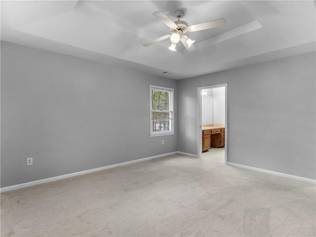 carpeted empty room with ceiling fan and a raised ceiling