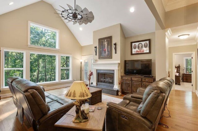 living room featuring ceiling fan, light hardwood / wood-style floors, a high end fireplace, high vaulted ceiling, and crown molding