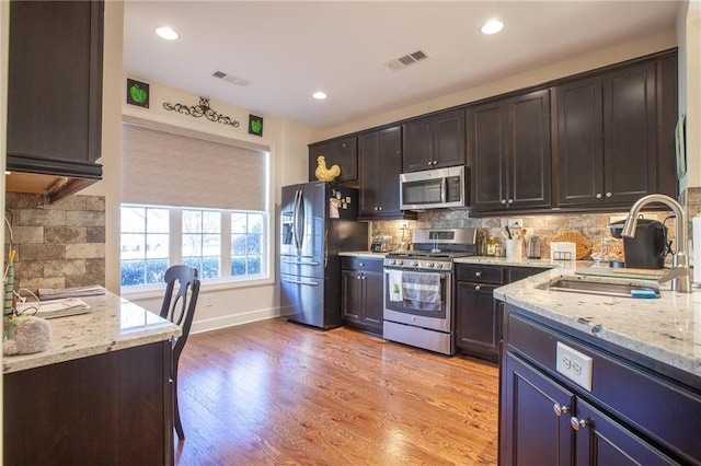 kitchen featuring sink, light stone countertops, tasteful backsplash, light hardwood / wood-style floors, and stainless steel appliances