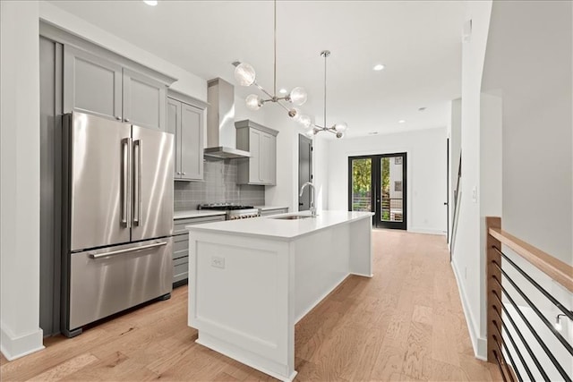 kitchen featuring tasteful backsplash, high end refrigerator, a kitchen island with sink, gray cabinetry, and wall chimney exhaust hood