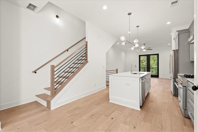 kitchen featuring pendant lighting, sink, light hardwood / wood-style flooring, a kitchen island with sink, and appliances with stainless steel finishes