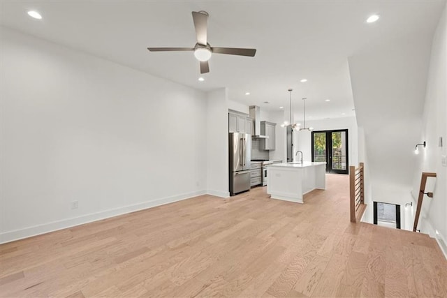 unfurnished living room featuring sink, ceiling fan with notable chandelier, and light hardwood / wood-style floors