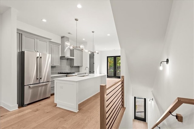 kitchen with pendant lighting, high quality fridge, gray cabinetry, sink, and a center island with sink