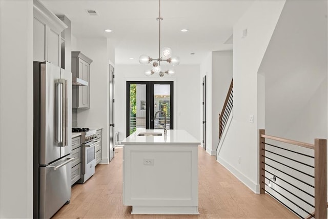 kitchen with light hardwood / wood-style floors, pendant lighting, sink, high end appliances, and a kitchen island with sink