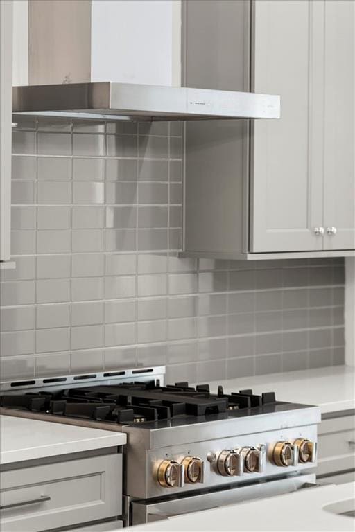 kitchen featuring white cabinets, backsplash, wall chimney range hood, and gas stove