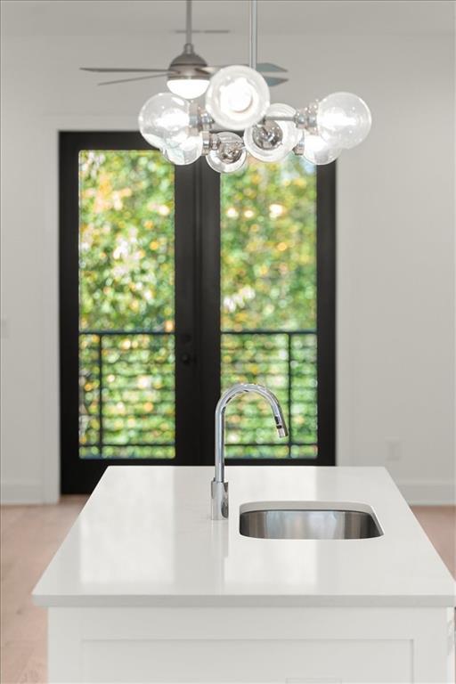 kitchen with white cabinetry, sink, hanging light fixtures, and a kitchen island with sink