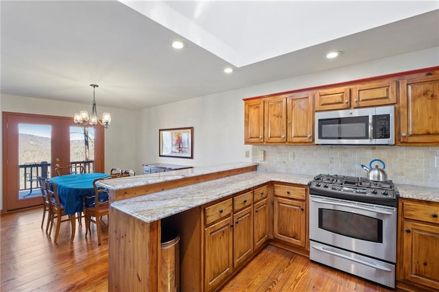 kitchen with brown cabinetry, a peninsula, hanging light fixtures, stainless steel appliances, and backsplash