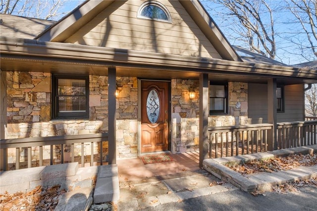 entrance to property with a porch, stone siding, and roof with shingles